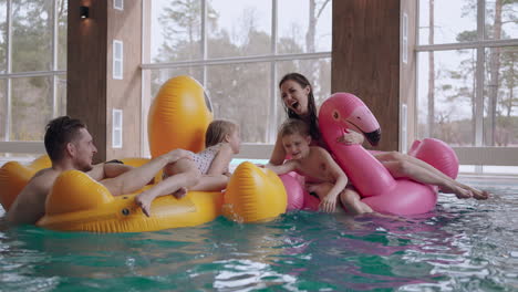 happy-family-with-two-little-children-are-resting-in-modern-spa-center-with-large-pool-thermal-bath